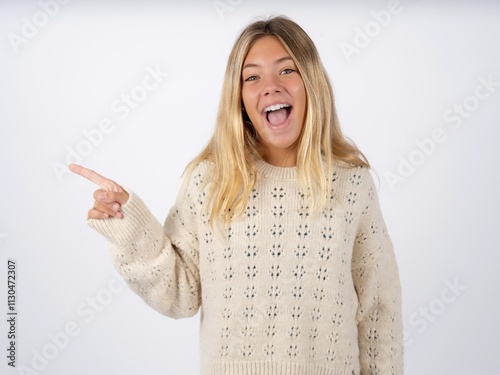 Beautiful teen girl wearing white sweater points aside on copy blank space. People promotion and advertising concept photo