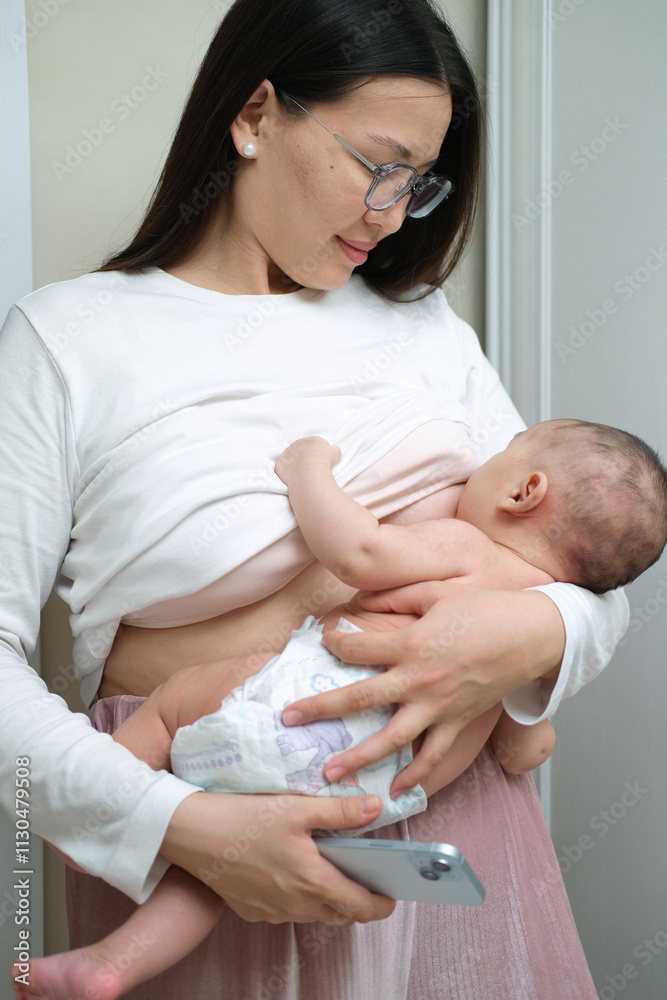 Obraz premium Beautiful young woman wearing white clothes is breastfeeding her baby at home, close-up back view.