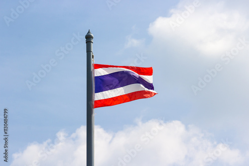 Small Thai flag fluttering proudly in the bright sunlight with puffy white clouds in the background