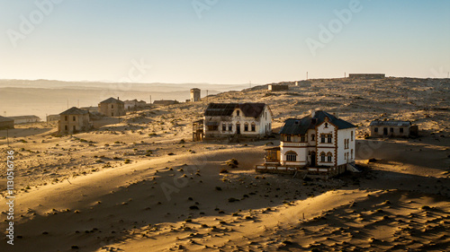 Clear dawn morning over the deserted diamond prospecting Kolmanskop village near Lüderitz in Namibia. Cloud low on horizon, first light on creeping dune sand in foreground. photo