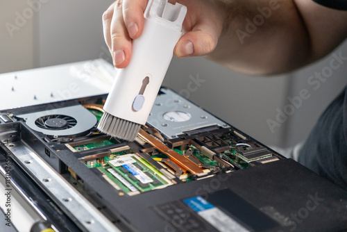 cleaning laptop motherboard using handheld vacuum cleaner, focus on copper heat pipes, RAM modules, and fan components photo