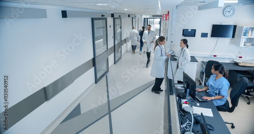 High Angle CCTV Shot with a Busy Hallway with Reception Desk of a Hospital Building, Diverse Female and Male Staff Members Walking, Working. Professional Nurses, Doctors and Personnel at Work