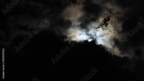 A captivating video of moonlight softly illuminating the night sky, casting an ethereal glow as it gracefully fades and reemerges through drifting thick clouds. photo