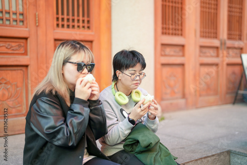 Two Chinese women in their 30s eating steamed buns in front of historical building in Jing'an District, Shanghai, China photo