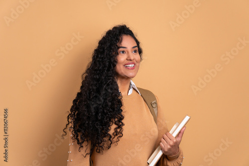 happy black young woman holding academy book and smiling in beige background. learn, school, student life concept. photo