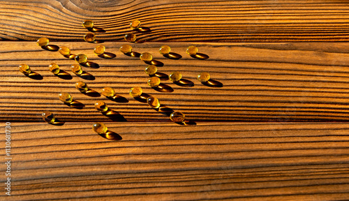 Vitamin D Capsules on Wooden Surface. Golden vitamin D capsules scattered on a textured wooden surface, illuminated by warm sunlight, casting sharp shadows.