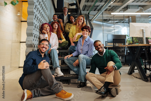 Start-up team posing on office stairs and floor, smiling at camera