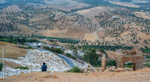 The Marinid Tombs or Merenid ruined monumental tombs on a hill above and north of Fes al-Bali, the old city of Fez, Fès, Fes, Morocco. Muslin cemetery. Woman sitting and watching.