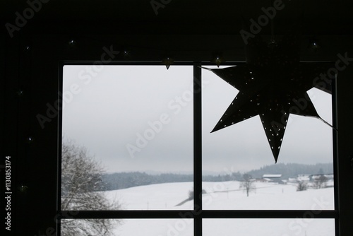 Gegenlichtaufnahme im Innenraum: Ein Fenster, mit zarter Lichterkette und einem Stern dekoriert. Im Hintergrund eine schneebedeckte Winterlandschaft. photo