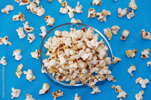 White fried airy popcorn in a transparent glass plate on a blue background