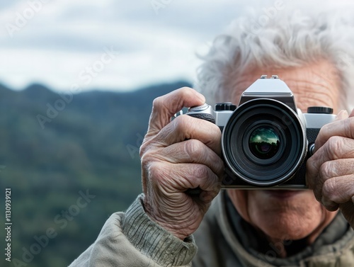 An older man holds a camera, capturing the scenic landscape, surrounded by nature and mountains. photo