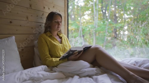 Woman reads a book while relaxing in a cabin in the forest.