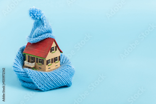 thermal insulation of buildings: old miniature model house with blue scarf and bobble hat, blue background photo