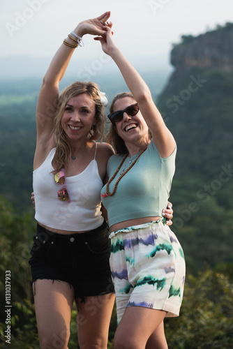 Two women tourists are raising arms and smiling with sigiriya in the background