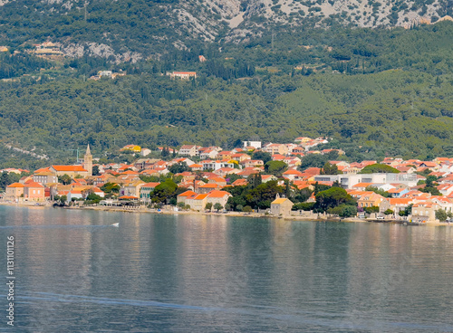 Orebic, Croatia - June 30, 2024: Church of Mary help of Christians towers over the town and hotels and restaurants on Adriatic Sea shoreline, all set in red roofed cityscape. Forested mountain flank i photo