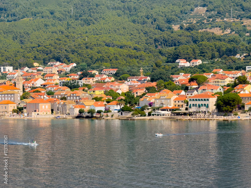 Orebic, Croatia - June 30, 2024: Church of Mary help of Christians towers over the town and hotels and restaurants on Adriatic Sea shoreline, all set in red roofed cityscape. Forested mountain flank i photo