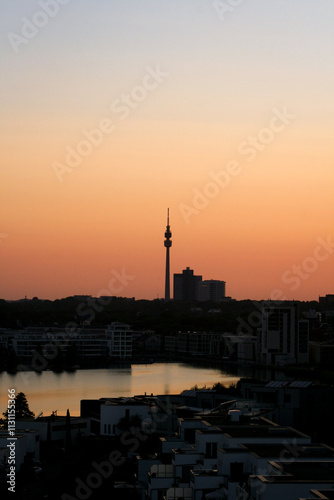 Sunset over Dortmund City skyline. City silhouette is between orange sky and its reflection in Phoenix See, vertical, Dortmund, North Rhine-Westphalia, Germany