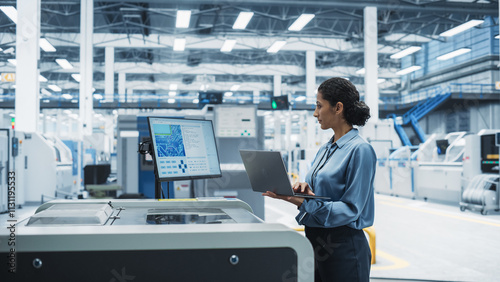 Hispanic Female Engineer Using Laptop To Control Soldering Jet Printer On Electronics Factory. Woman Working On Production Of Innovative Circuit Boards For Artificial Intelligence Systems.