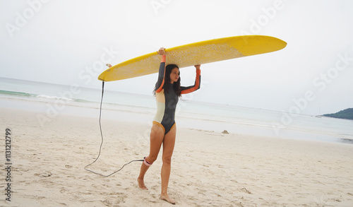 Young woman wearing tight wetsuit is going to surfboard at beautiful beach photo