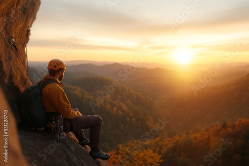 Climber watches sunset from rocky ledge in serene mountain landscape during autumn photo