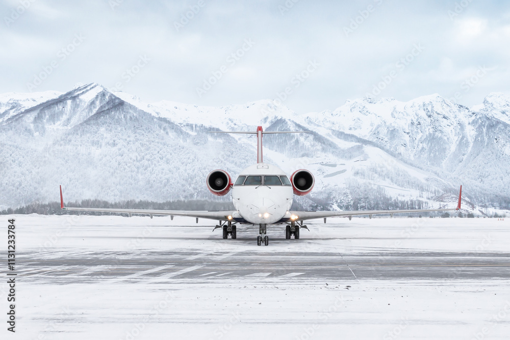 Naklejka premium Front view of a passenger regional jet taxiing at winter airport on the background of high scenic mountains