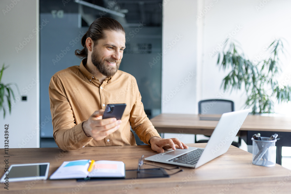 Fototapeta premium A modern office worker multitasking using a phone and laptop at a wooden table in an office. The scene conveys productivity and professional engagement with technology in a corporate environment.