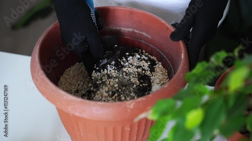 Hands preparing soil by mixing fertilizer with potting mix in large terracotta plant pot