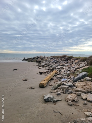 Beach shoreline, rocks on the levy with big cloud sky