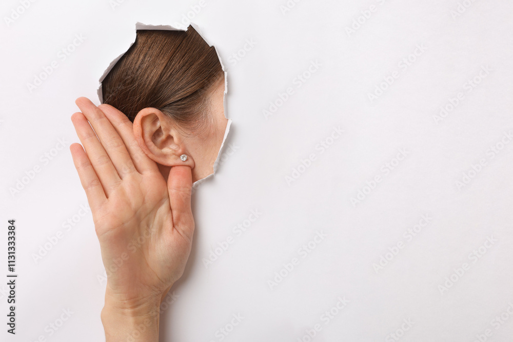 Εκτύπωση καμβά Woman showing hand to ear gesture through hole in white paper, closeup