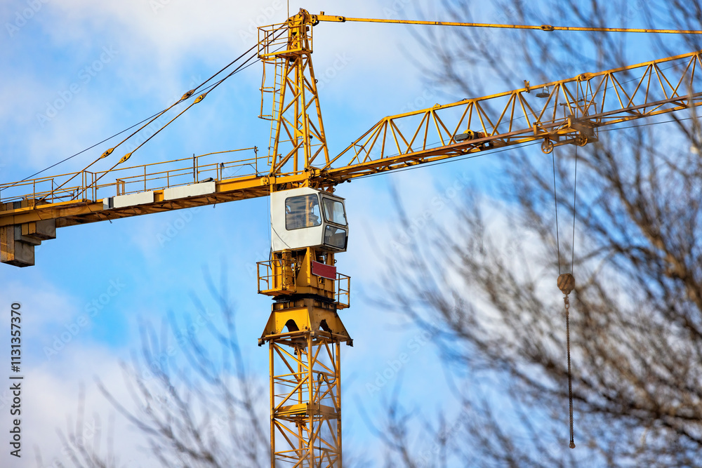Construction crane stands tall against a blue sky amidst winter trees in a bustling city