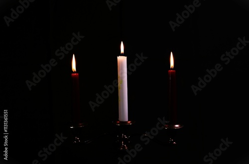 three sad red and white burning candles in a glowing candlestick on a black background