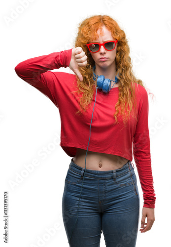 Young redhead woman wearing headphones with angry face, negative sign showing dislike with thumbs down, rejection concept