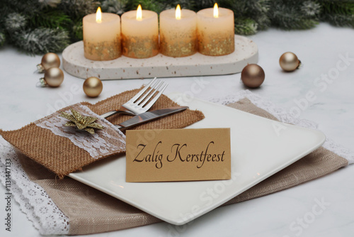 Table decoration for Christmas. Candles with fir branches and a table setting. The text Zalig Kerstfeest is written on a place card. photo