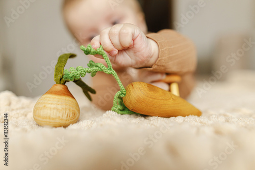 Adorable happy baby boy playing with wooden toys on bed. Safe Childhood. Portrait of cute child infant teething with eco toys photo