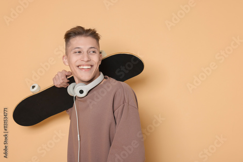 Happy man with skateboard and headphones on beige background. Space for text