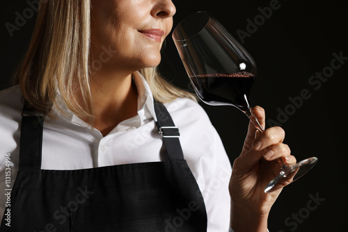 Professional sommelier tasting red wine in glass on black background, closeup photo