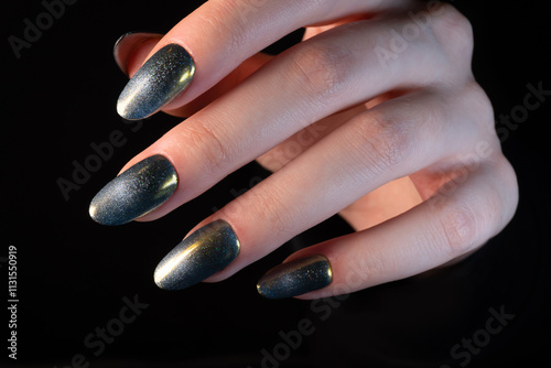 A stylish manicure in dark metallic tones with golden highlights of cat-eye polish creates a contemporary and striking look.