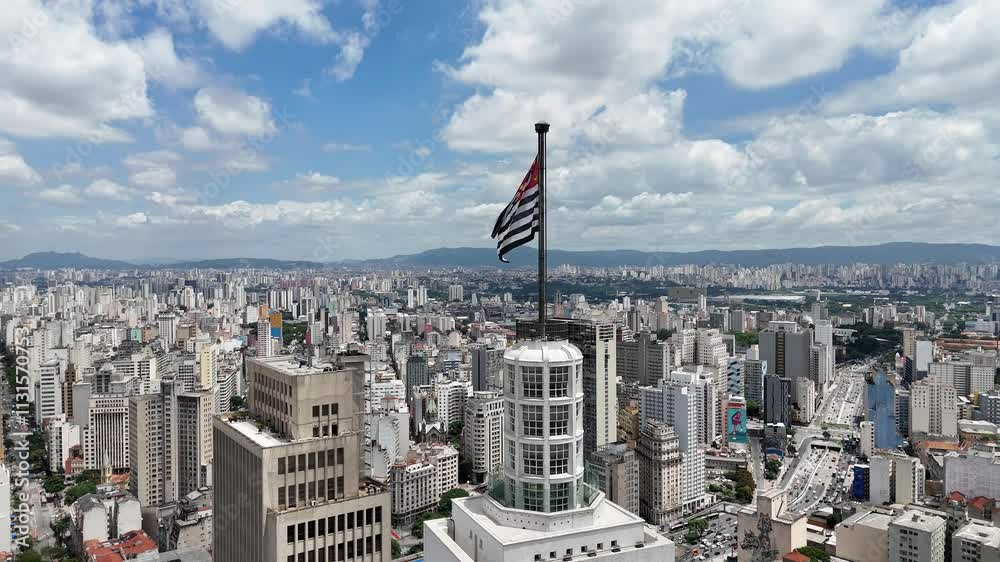 Vídeo da bandeira da cidade de São Paulo no topo do Edifício Altino Arantes, destacando o icônico prédio e a paisagem urbana da cidade, com vista para o horizonte e o skyline