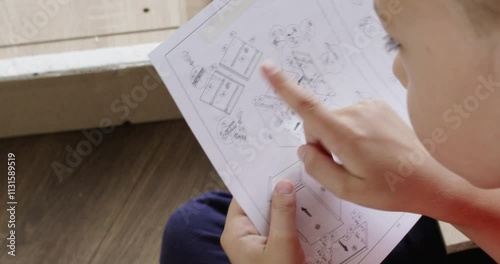 Young boy carefully studying assembly instructions while putting together a piece of furniture. Focused on the task, he engages in a hands on diy project, showcasing learning and skill development