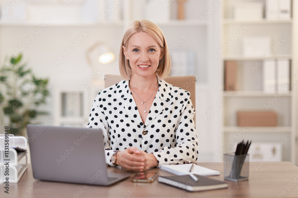 © New Africa - Portrait of smiling middle aged woman at table in office