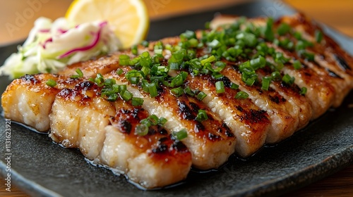 Close-up of grilled fish fillet, sliced and seasoned with chopped scallions, served with a side of coleslaw and lemon wedge.