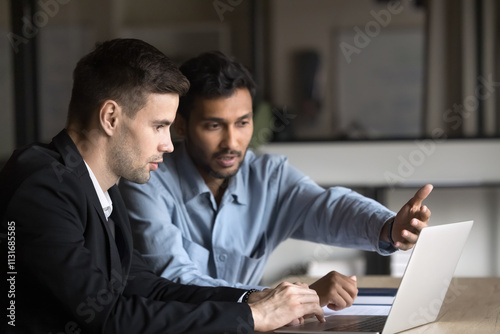 Two Indian and Caucasian businessmen, partners discussing online project progress, reviewing financial reports or budgets. Sales manager presenting new product or service options to client on laptop