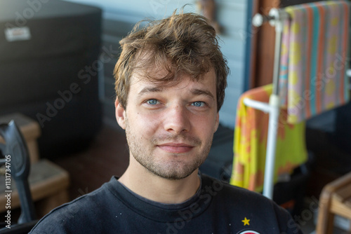 A close-up of a young man's face with vibrant blue eyes looking upward. The photo captures fine skin details, soft natural light, and a dreamy, introspective mood with a blurred green background