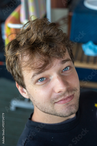 A close-up of a young man's face with vibrant blue eyes looking upward. The photo captures fine skin details, soft natural light, and a dreamy, introspective mood with a blurred green background