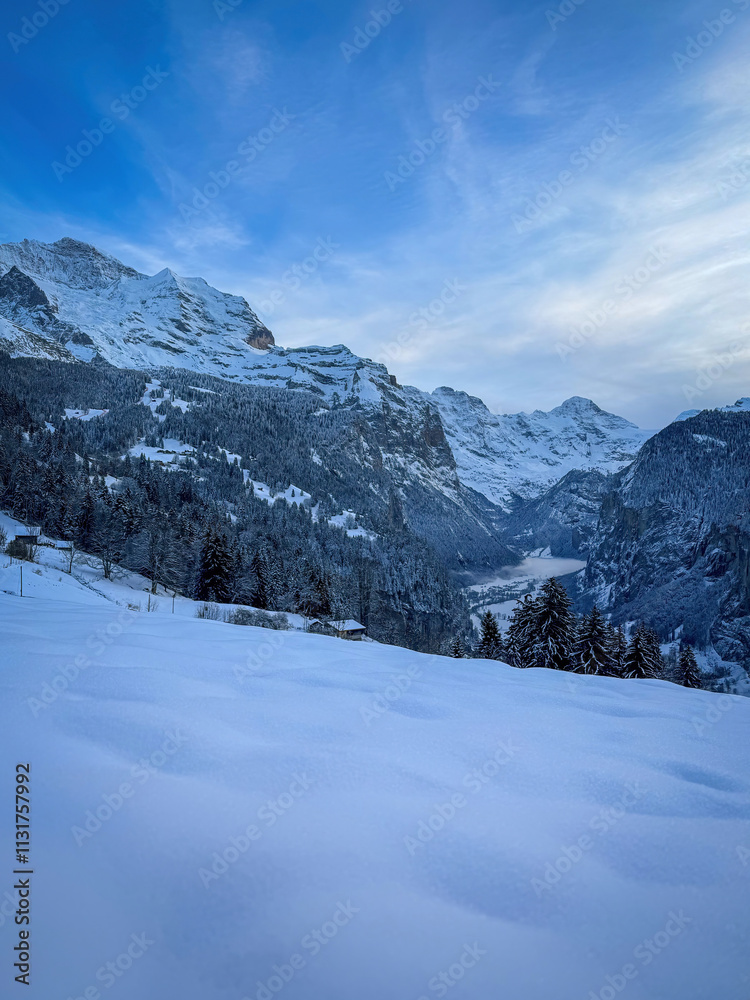 Panoramic view of Lauterbrunnen Valley, Switzerland seen from Wengen with snowcovered Breithorn (middle) and Jungfrau (left) mountain in winter against blue sky with clouds
