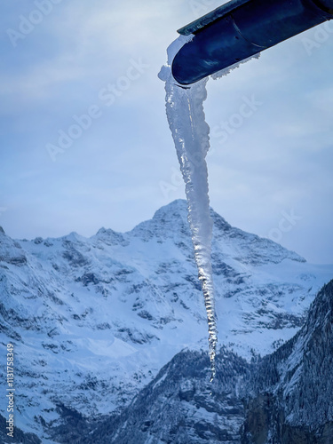 Obraz na płótnie Icicle coming out of a gutter infront of snowcapped Breithorn mountain in Switzerland in winter against cloudy sky w salonie