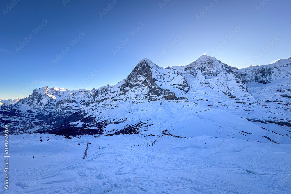 Panoramic view of famous snowcoverd mountains Eiger and Moench (from left to right) in Switzerland with Grindelwald and Wetterhorn (far left) in winter early in the morning against blue sky