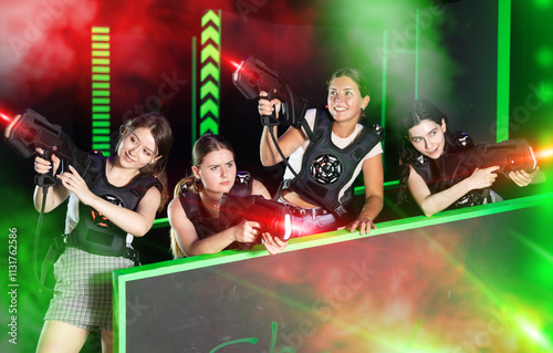 Four cheerful positive girlfriends playing enthusiastically laser tag in dark room photo