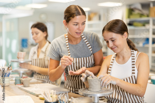 Young female teacher explains to teenage girl student how to make ceramics in workshop