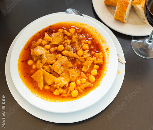 Beef stomach stew, potatoes, seasonings, chickpea. Traditional dish of Russian cuisine prepared in national restaurant for guests of institution, served in clay tureen with slices of bread baguette photo